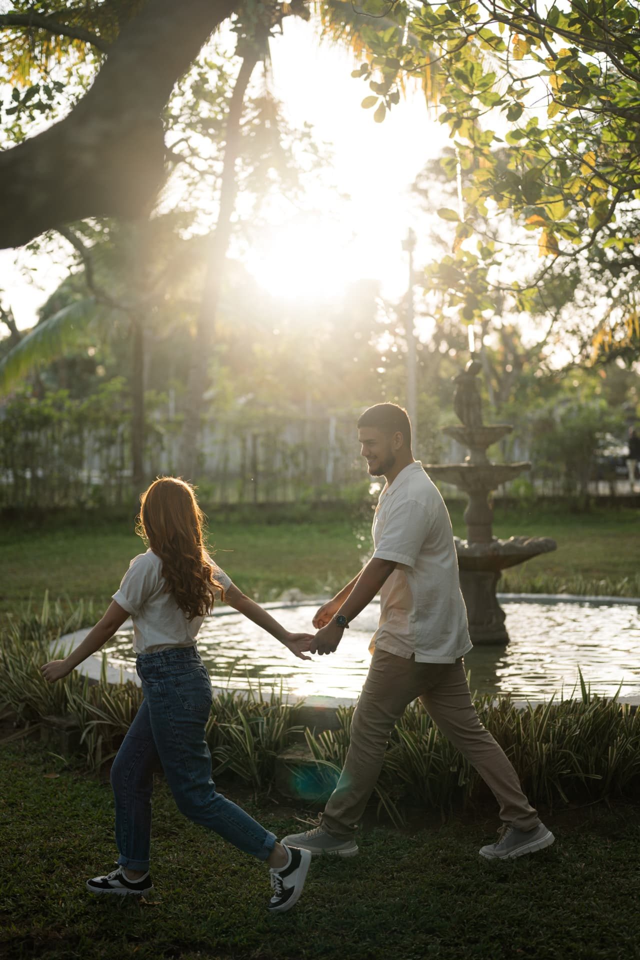 Casal caminhando de mãos dadas perto da fonte do jardim ao pôr do sol