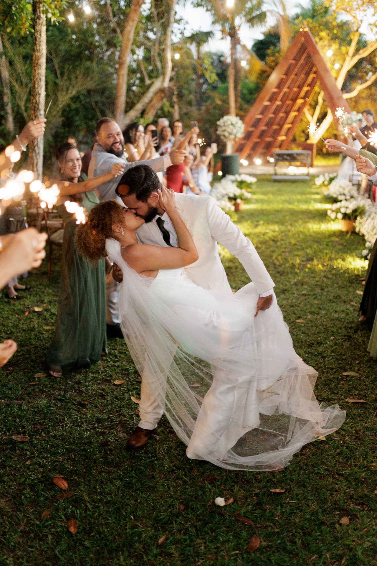 Noivos se beijando sob chuva de faíscas na saída da festa